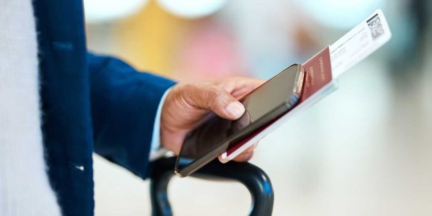 A gentleman holding his phone and passport with luggage at the airport | Class P permit guide for UN Diplomatic, and International Organization Staff | Njaga & Co. Advocates Immigration lawyer services